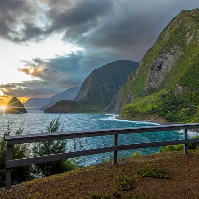A lookout with a fenced area before a cliff overlooking the ocean and pali