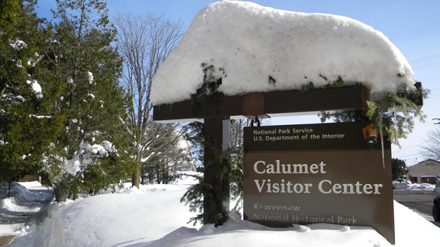 A sign covered on the top with snow reading "Calumet Visitor Center."