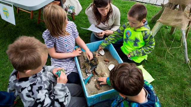 Kids gather around a container with sand and objects.