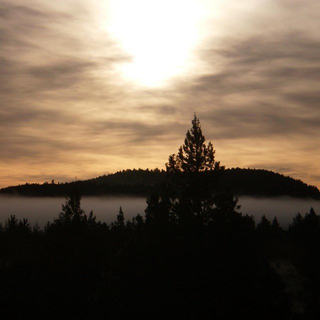Sunset in cloudy sky over mountain and trees at Lava Beds National Monument