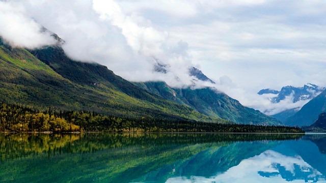 Image of calm lake with reflections and mountains in the background.