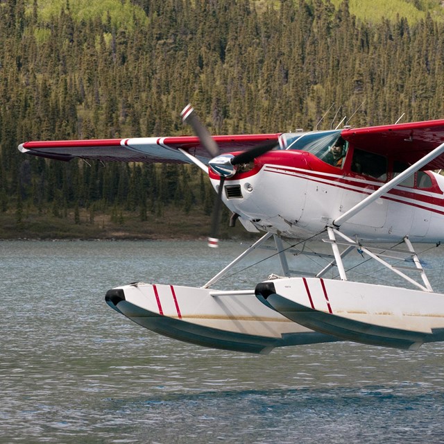 A red and white floatplane takes off from a lake