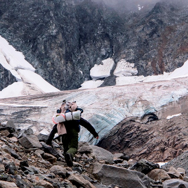 A hiker approaches a small glacier surrounded by rock