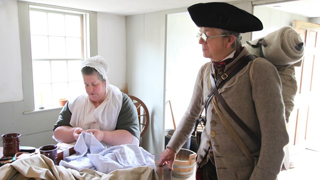 Park volunteers dressed in Colonial clothing work on a sewing project and present to a group
