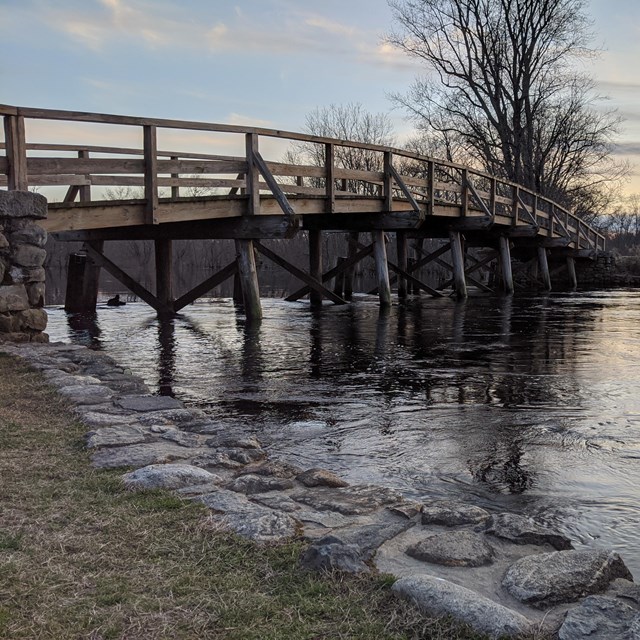 A wooden bridge spans a small river at sunset
