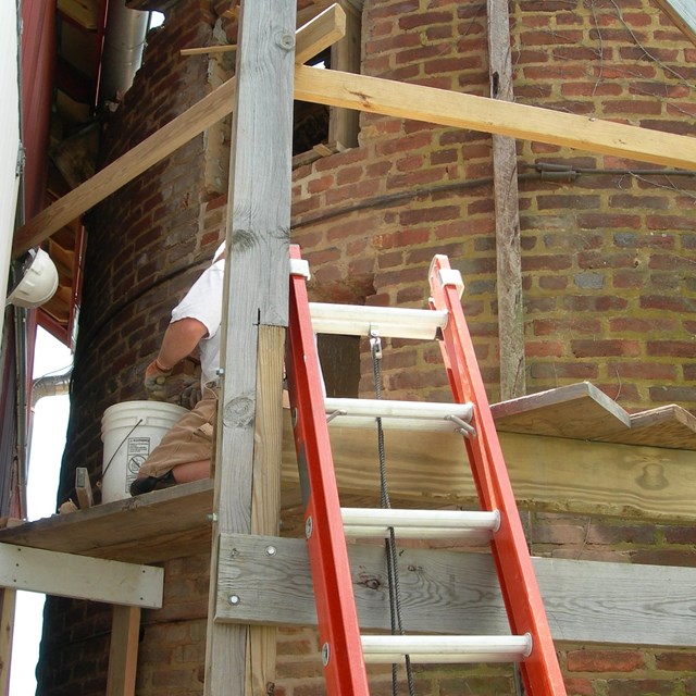 A worker repairs brickwork on a brick silo.