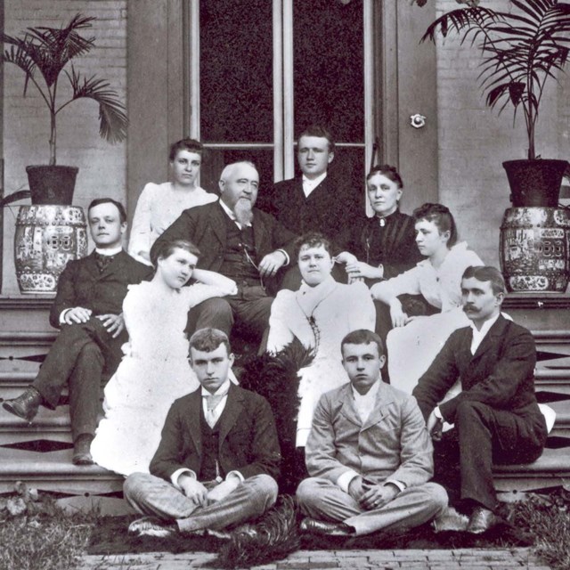Group of people seated on the front steps of a large house.