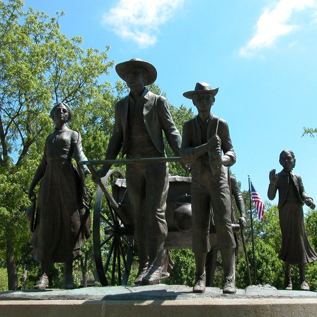 Bronze statue of pioneer people, pulling a two-wheeled, wooden hand cart.