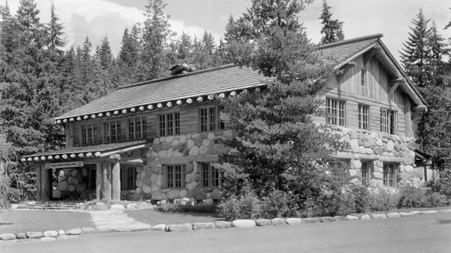 Historic photo of a two story wood and stone building next to a dirt road. 