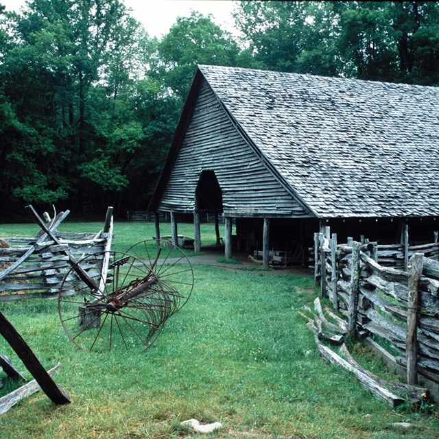 Green grass and trees surround a wooden structure with roof but no sides, and wooden fencing.