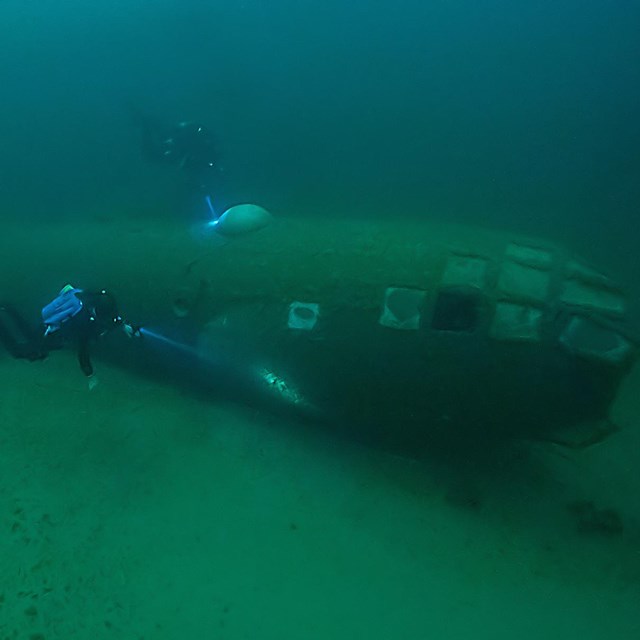 Two divers near submerged B-29 fuselage.