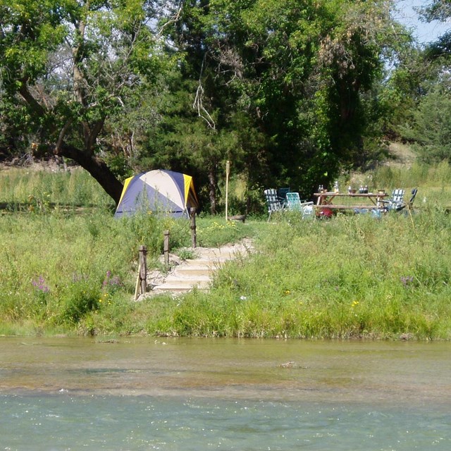 A stairway into a river with tents in the background on a green shore