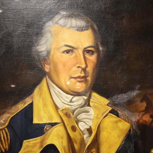 A man in a white wig dressed in a blue coat with buff lining. 