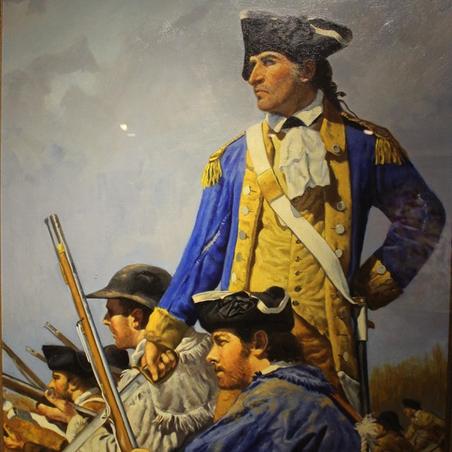 A man in a blue coat with a drawn sward stands among other kneeling men. 
