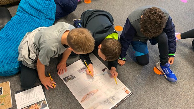 Three students on the ground look at a map while filling out a worksheet 