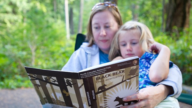 A child sits with a parent while reading the Junior Ranger workbook