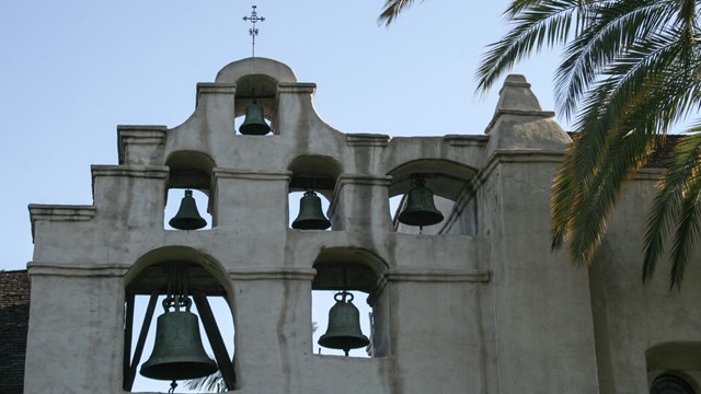 A white spanish mission's bellfry next to a palm tree.