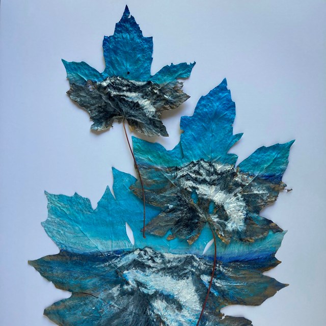 Three large maple leaves with increasingly receded views of a glacier painted on them.