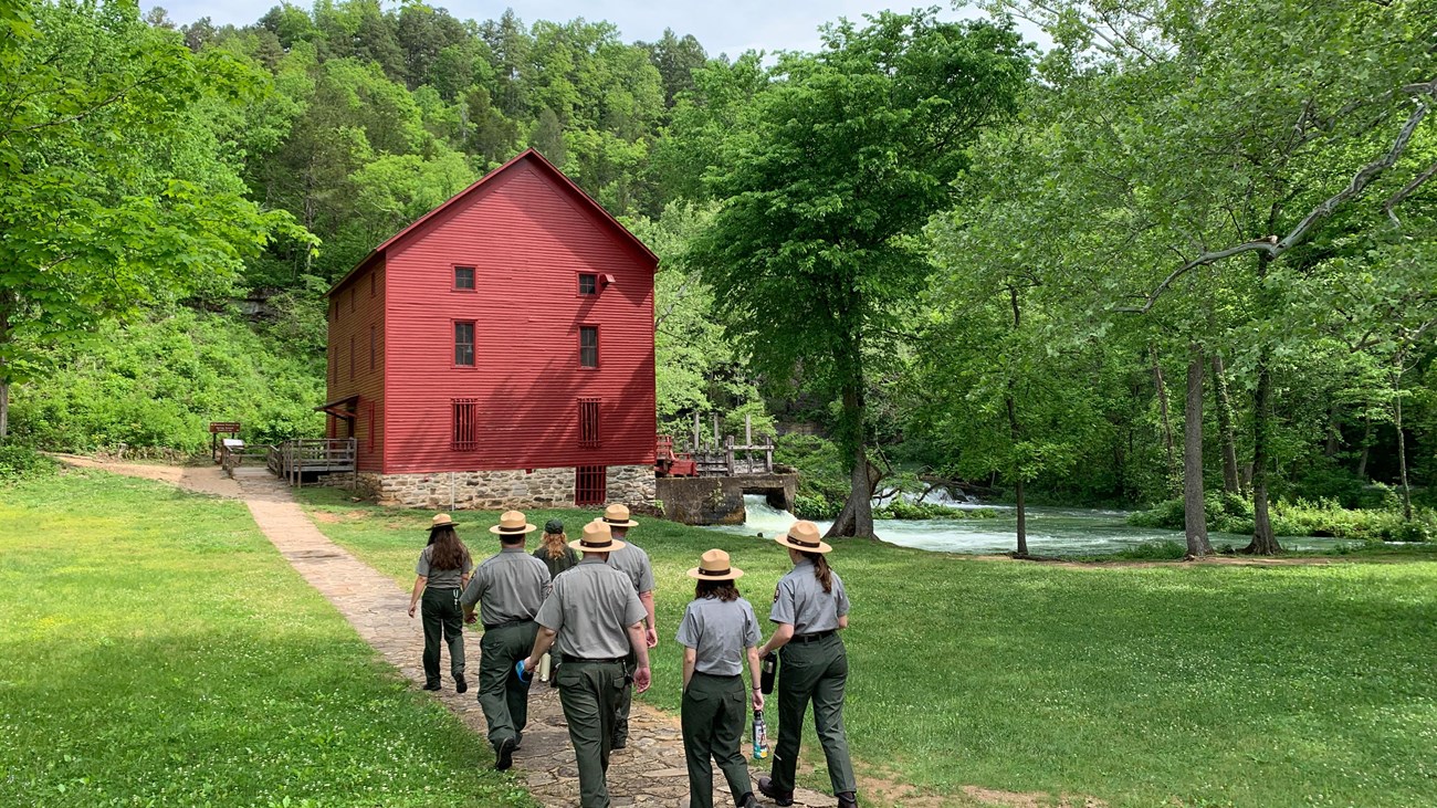 A group of park rangers walk towards a red mill.