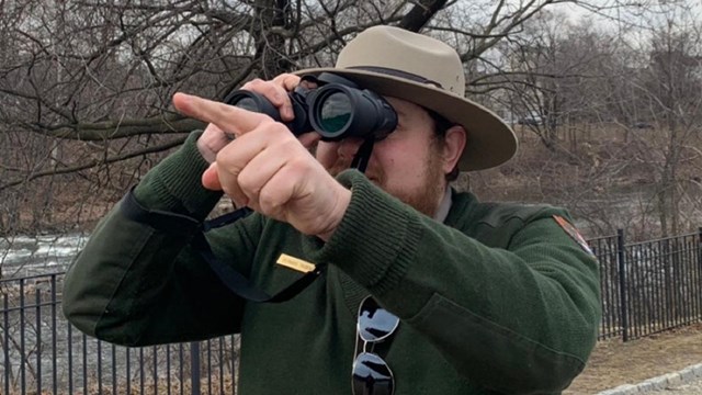 A park ranger holds binoculars to their eyes and points forward