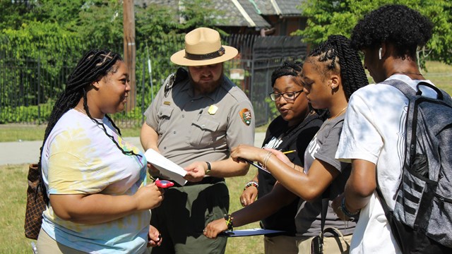 A park ranger works with high school students with outdoor activity sheets