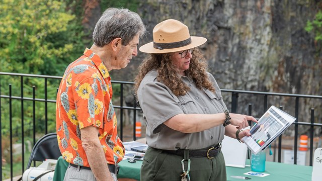 A park ranger holds printed resources for a visitor standing beside her