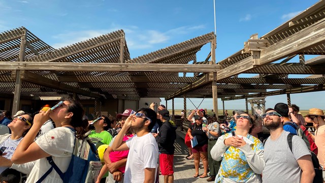 A group of people wearing solar glasses watch a solar eclipse. 