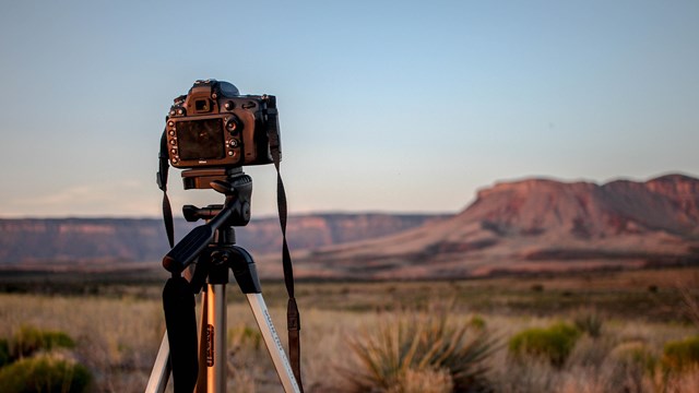 Image of a camera on a tripod with a desert landscape in the background. 
