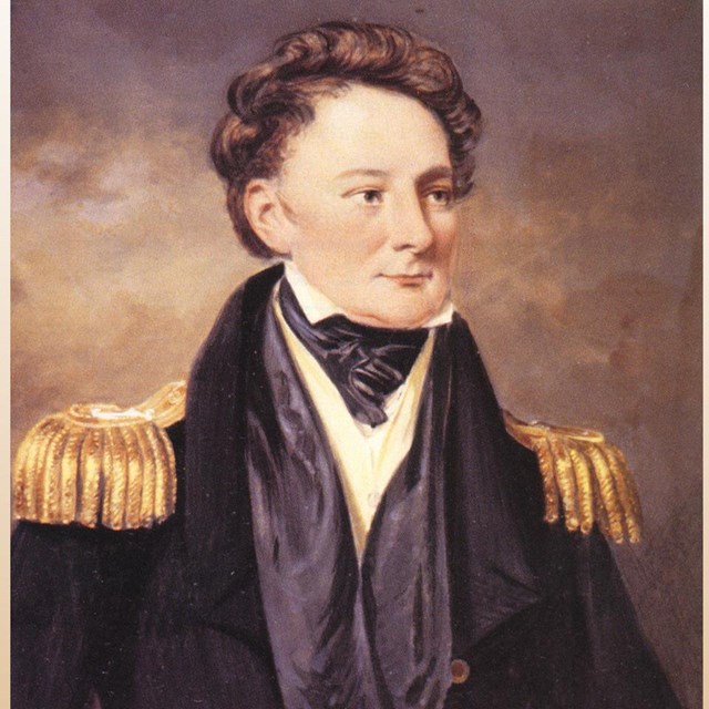Man with wavy brown hair in a dark blue jacket with gold epulets, a blue ascot under a white shirt a