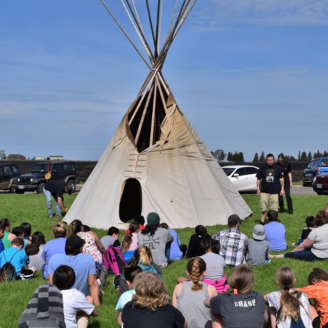 A photo of a class of students outside of a tipi