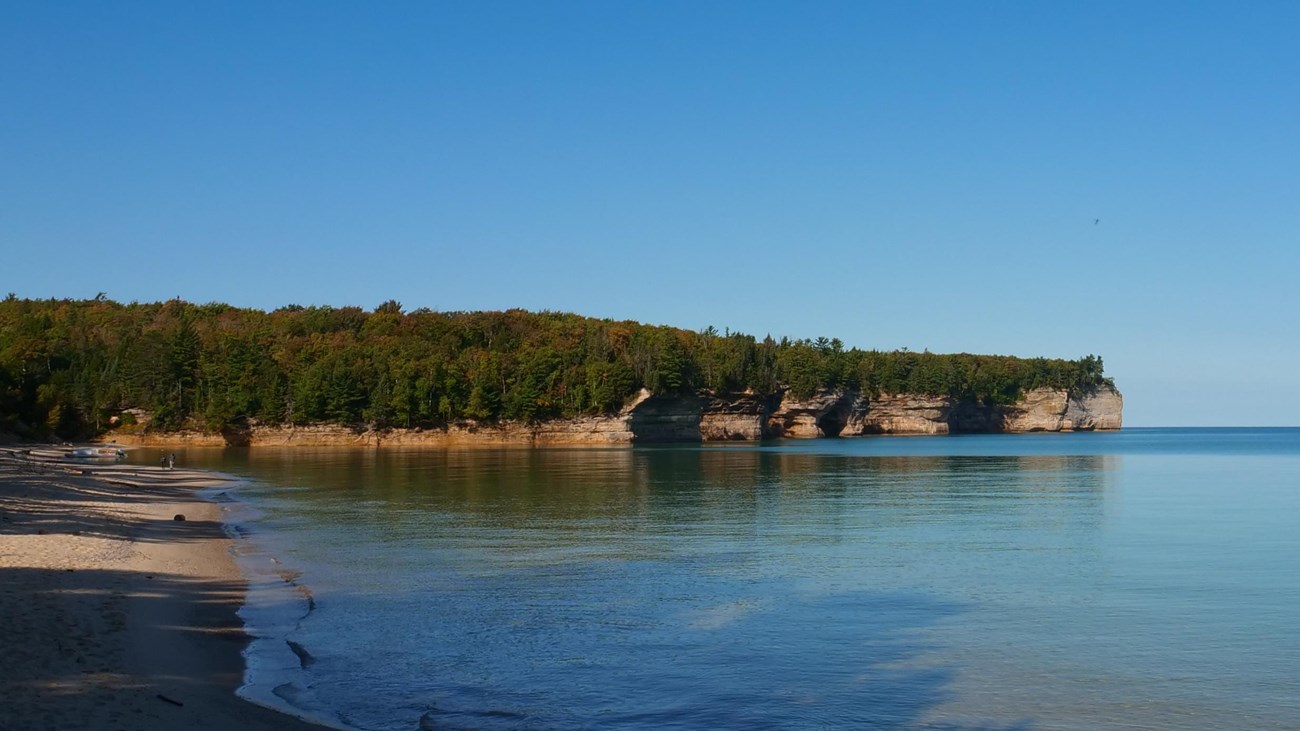 Sandstone cliffs rise out of a calm Lake Superior