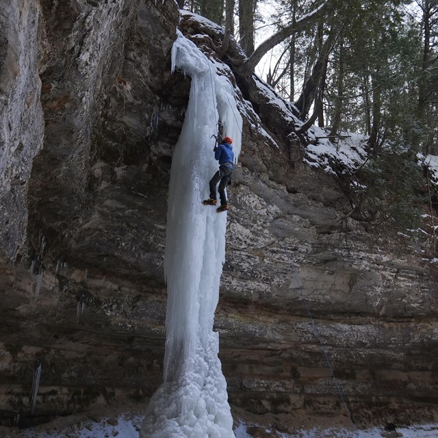 A person in a blue jacket climbs a tall ice column