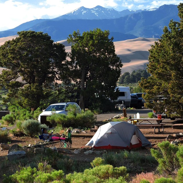 Campground with tent, trailer, and picnic tables with sand dunes and mountains in background 