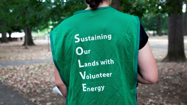 the back of a vest a person is wearing spells out sustaining our lands with volunteer energy