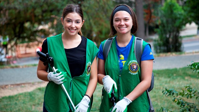 two people smiling at the camera; they are green wearing volunteer vests