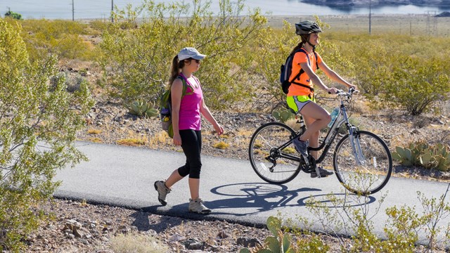 A person walks on a paved trail next to a bicyclist 