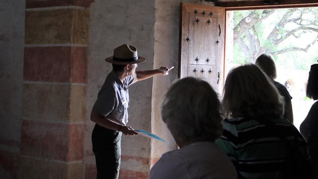 Female Park Ranger points through a doorway while talking to a group.