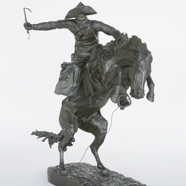 A bronze statue of a cowboy riding a horse.