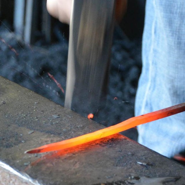 Blacksmith hammering orange-hot nail rod