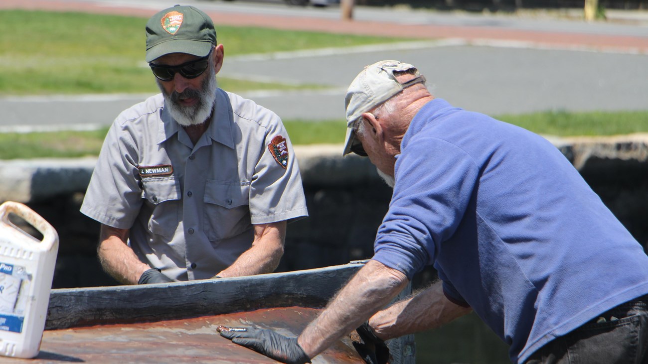 A park ranger works with a volunteer to preserve a small boat.