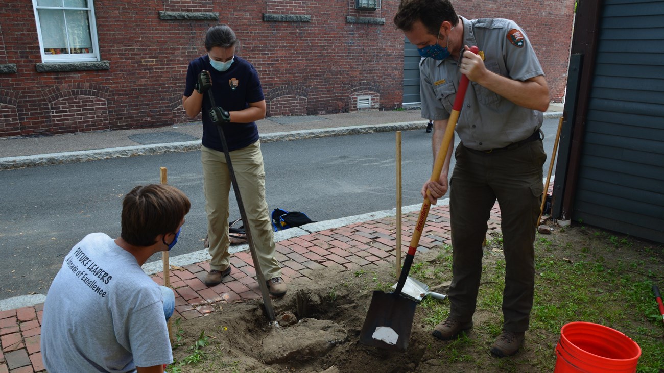 National Park Service staff speak with a member of the future leaders program while digging a hole.