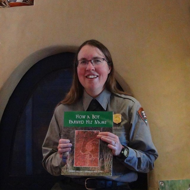 A ranger sits in front of a fireplace holding the book, 