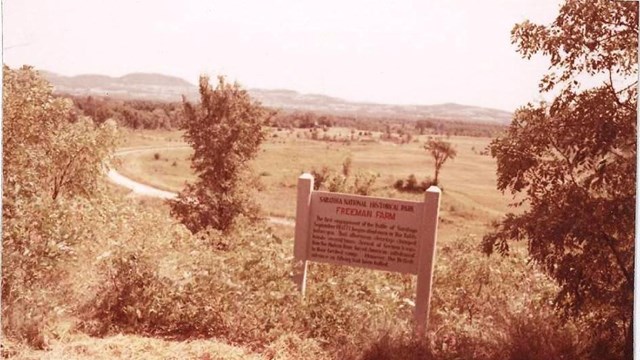 A sign on an overlook with rolling green hills says "Saratoga National Historical Park."