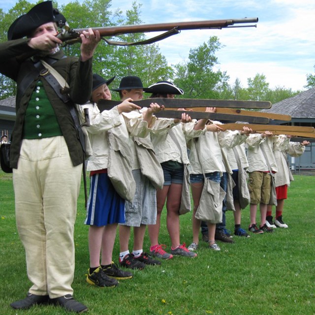 An 18th century soldier conducting musket drill with a group of students
