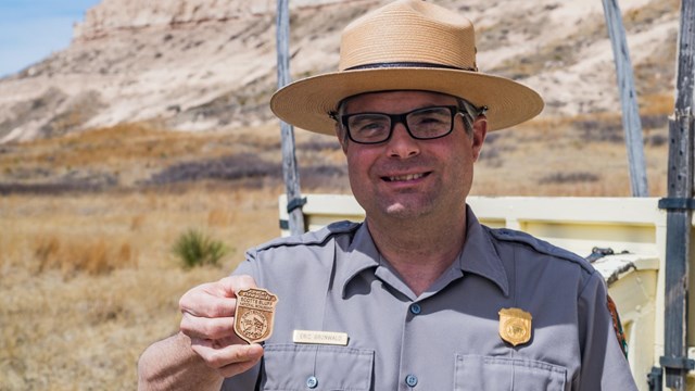 A park ranger holds out a Junior Ranger badge. 