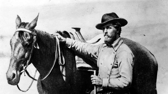 A black and white photo of a man standing next to a horse.