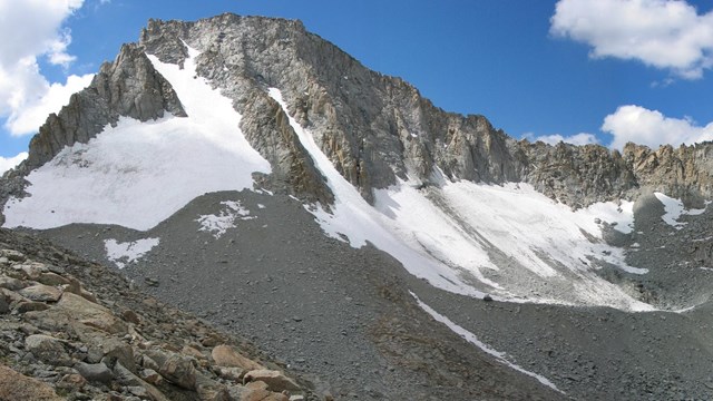 The steep rocky face of a mountain with icy remnants of a glacier.