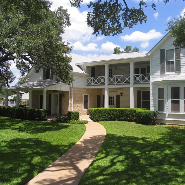 Path leading to a large, white house with tidy landscaping