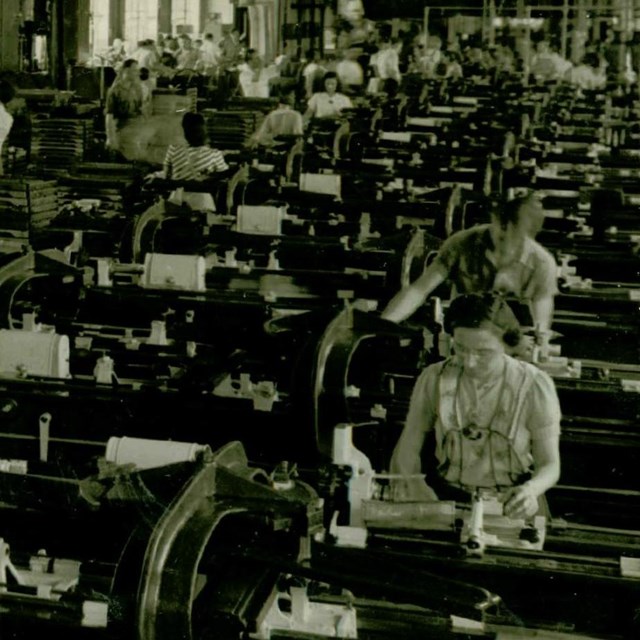A black and white photo showing rows of men and women working at machines. 