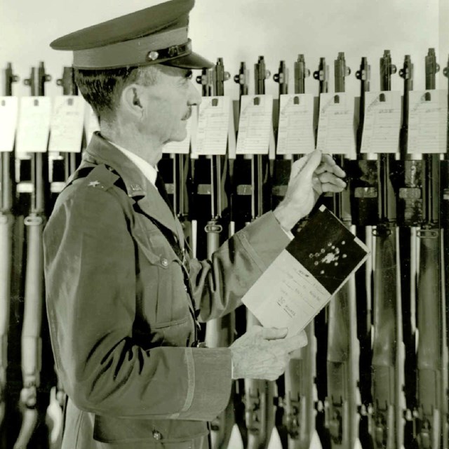 A black and white photo of general looking at different firearms. 